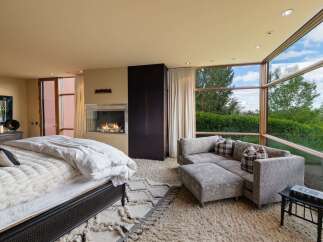 Experience luxury living in this master suite featuring a modern gas fireplace and expansive floor-to-ceiling windows that offer breathtaking views of the surrounding greenery.