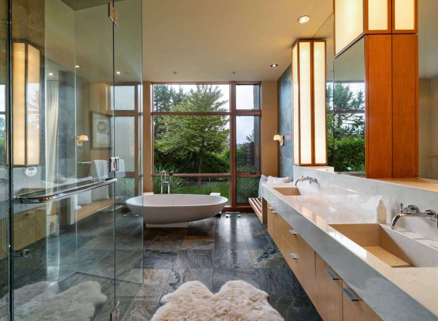 Experience luxury in this modern bathroom featuring a freestanding soaking tub with a stunning garden view through a large picture window.