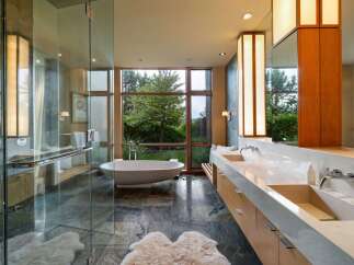 Experience luxury in this modern bathroom featuring a freestanding soaking tub with a stunning garden view through a large picture window.