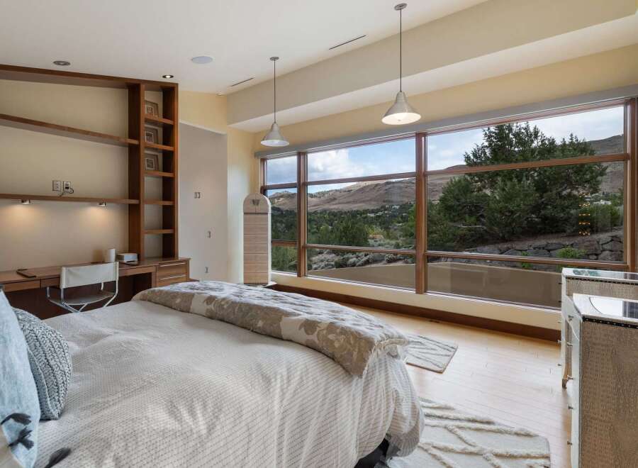 Experience breathtaking mountain views from this luxurious bedroom, featuring a spacious built-in desk and shelving unit perfect for a home office.