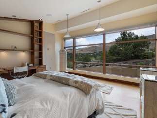 Experience breathtaking mountain views from this luxurious bedroom, featuring a spacious built-in desk and shelving unit perfect for a home office.
