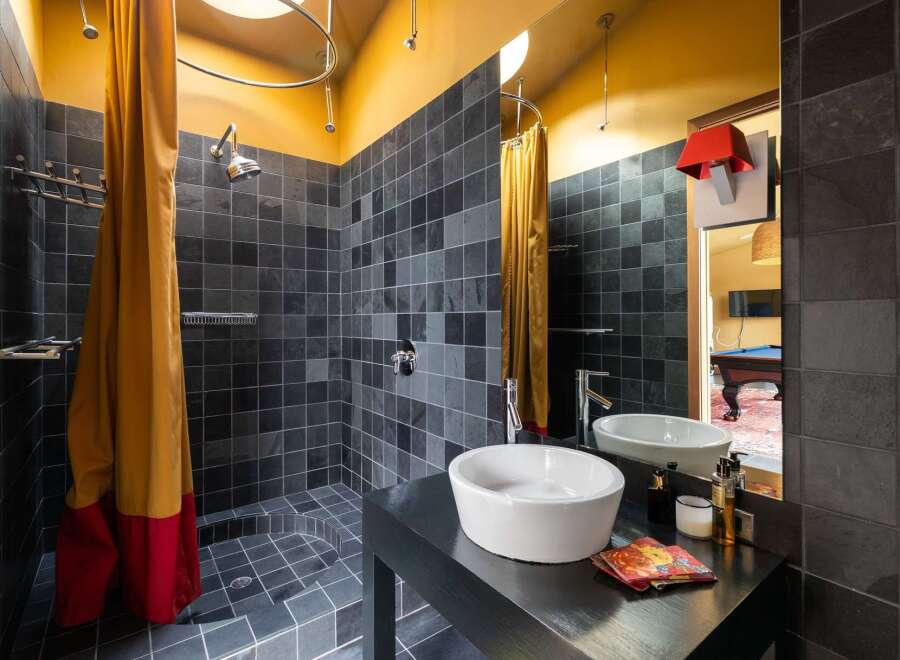 Experience modern luxury in this unique bathroom featuring a spacious walk-in shower with dark slate tiles and a vibrant mustard and red shower curtain.