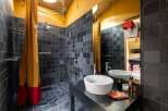 Experience modern luxury in this unique bathroom featuring a spacious walk-in shower with dark slate tiles and a vibrant mustard and red shower curtain.
