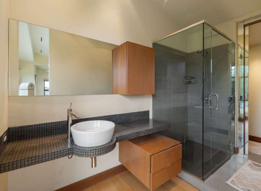 This modern bathroom features a sleek vessel sink atop a mosaic tile vanity, complemented by a floating wood cabinet and a spacious glass-enclosed shower with grey tile walls.