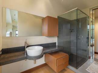 This modern bathroom features a sleek vessel sink atop a mosaic tile vanity, complemented by a floating wood cabinet and a spacious glass-enclosed shower with grey tile walls.