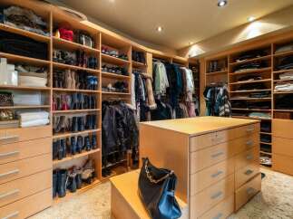 Step into this luxurious walk-in closet, meticulously organized with custom wood shelving and drawers.