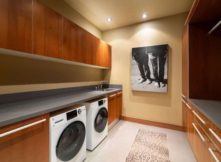 This modern laundry room features sleek cherry wood cabinetry and a durable gray countertop, providing ample storage and workspace.