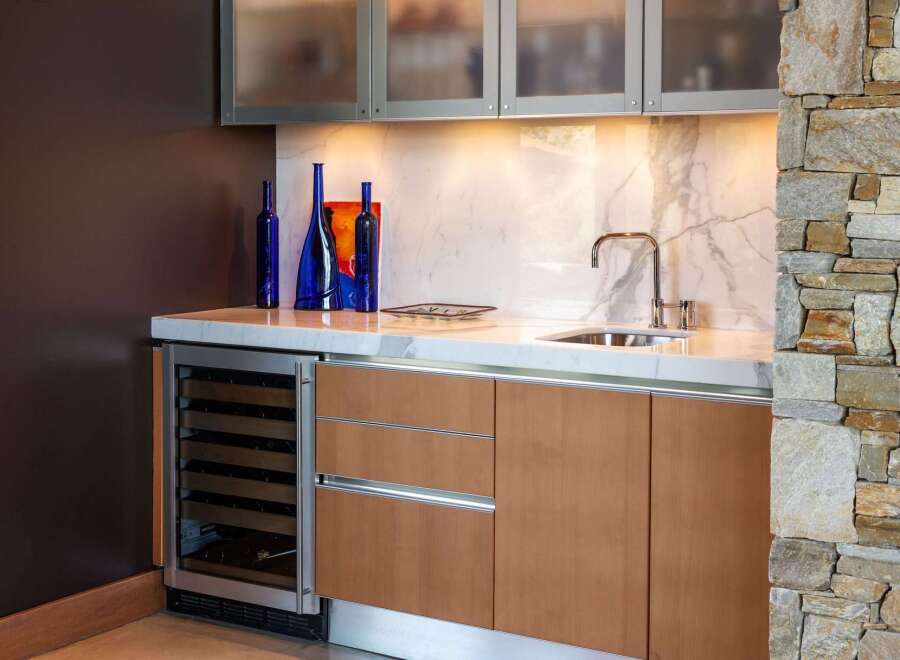 This modern wet bar features a sleek wine cooler, ample cabinet storage, and a marble countertop.