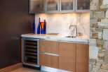 This modern wet bar features a sleek wine cooler, ample cabinet storage, and a marble countertop.