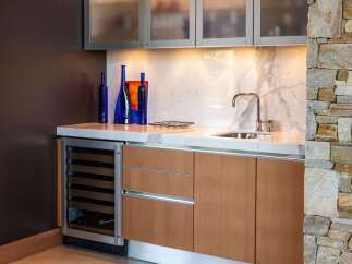 This modern wet bar features a sleek wine cooler, ample cabinet storage, and a marble countertop.