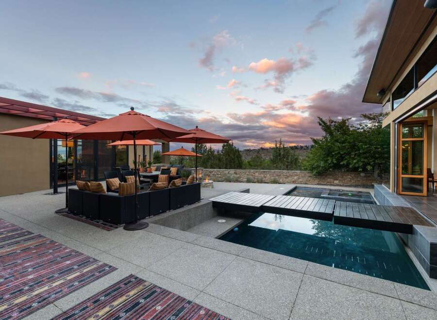 Experience luxurious outdoor living with this stunning patio featuring a modern pool and spa, complemented by comfortable seating under vibrant orange umbrellas.