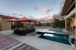 Experience luxurious outdoor living with this stunning patio featuring a modern pool and spa, complemented by comfortable seating under vibrant orange umbrellas.