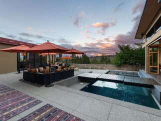 Experience luxurious outdoor living with this stunning patio featuring a modern pool and spa, complemented by comfortable seating under vibrant orange umbrellas.