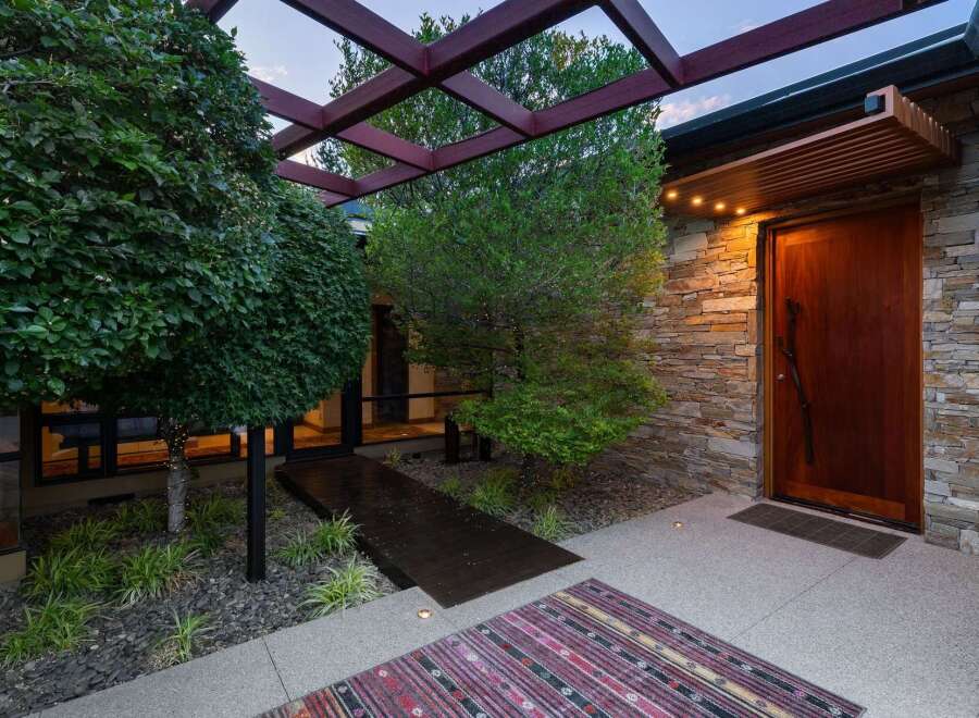 Experience modern luxury with this stunning entryway, featuring a striking wooden door set against a natural stone accent wall.