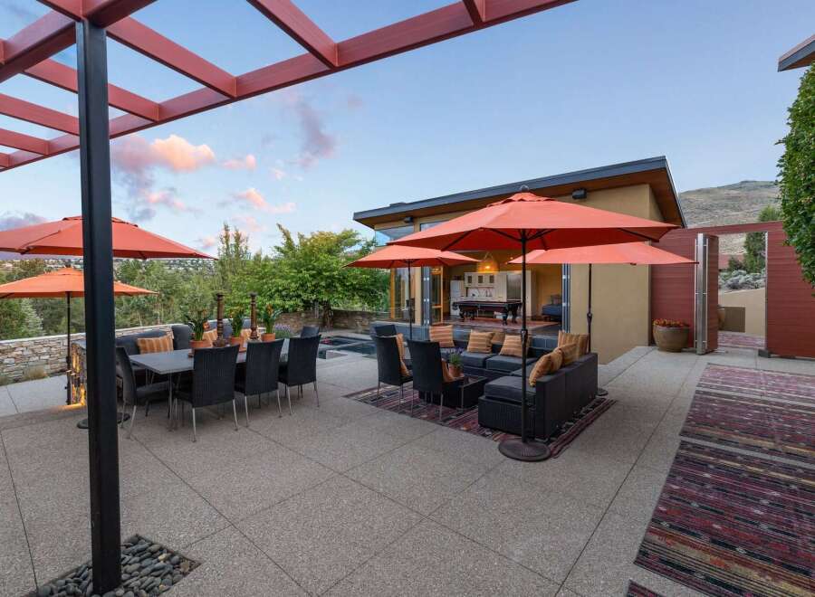 Experience luxurious outdoor living with this stunning patio featuring a spacious dining area under a pergola and a comfortable lounge space with orange umbrellas for shade.