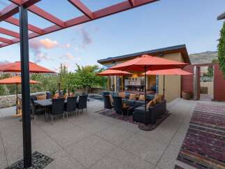 Experience luxurious outdoor living with this stunning patio featuring a spacious dining area under a pergola and a comfortable lounge space with orange umbrellas for shade.