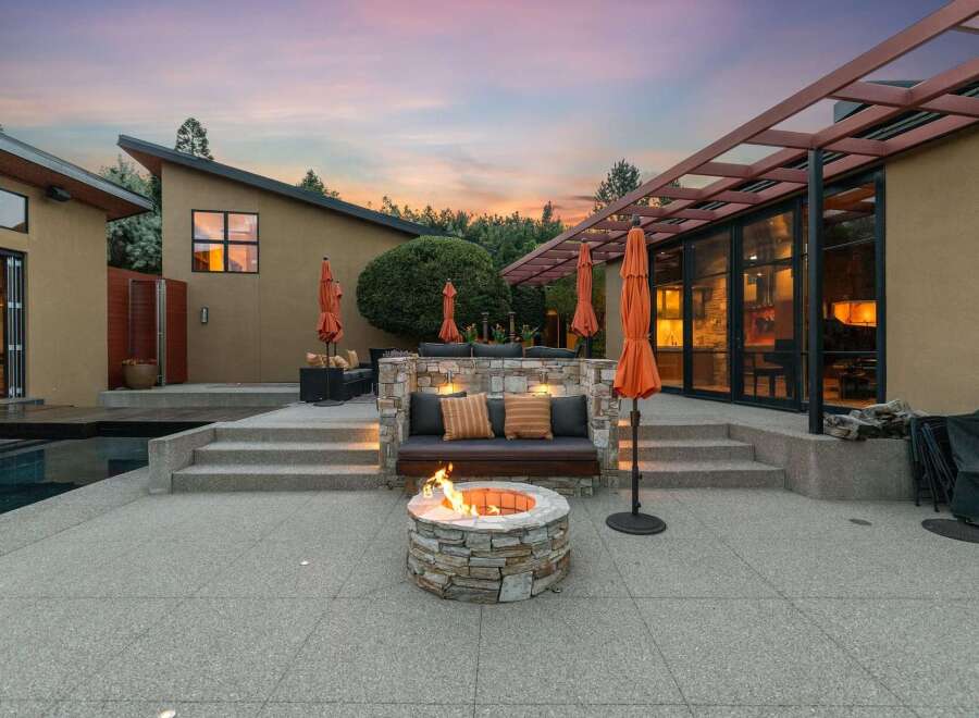 Experience luxurious outdoor living with this stunning patio featuring a built-in stone seating area, a cozy fire pit, and vibrant orange umbrellas.