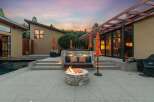Experience luxurious outdoor living with this stunning patio featuring a built-in stone seating area, a cozy fire pit, and vibrant orange umbrellas.
