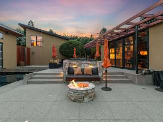 Experience luxurious outdoor living with this stunning patio featuring a built-in stone seating area, a cozy fire pit, and vibrant orange umbrellas.