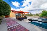 Experience luxurious outdoor living with this stunning patio featuring a modern sectional sofa, vibrant orange umbrellas, and a refreshing swimming pool.