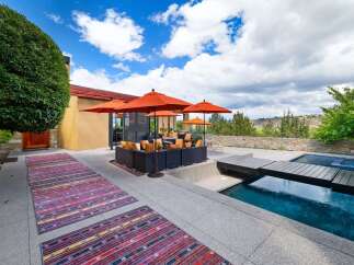 Experience luxurious outdoor living with this stunning patio featuring a modern sectional sofa, vibrant orange umbrellas, and a refreshing swimming pool.