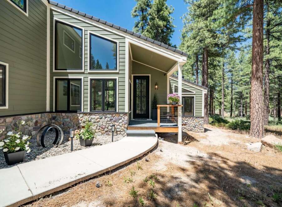Nestled amidst tall pine trees, this charming home features a striking modern design with a mix of green siding and natural stone accents.