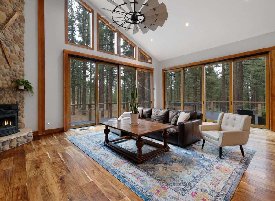 Experience rustic elegance in this stunning living room, featuring a grand stone fireplace and expansive windows that bring the outdoors in.