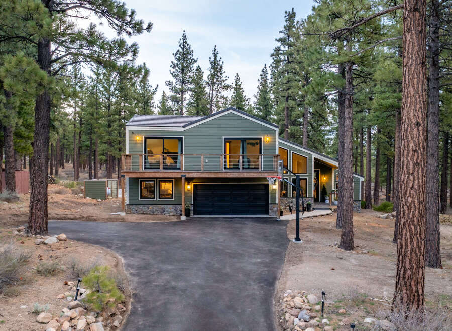 Nestled amidst tall pine trees, this modern home offers a serene retreat with its striking green exterior and expansive windows.