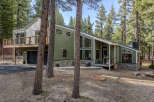 Nestled among tall pines, this modern mountain home boasts a striking green exterior with stone accents and a multi-level deck perfect for enjoying the serene surroundings.