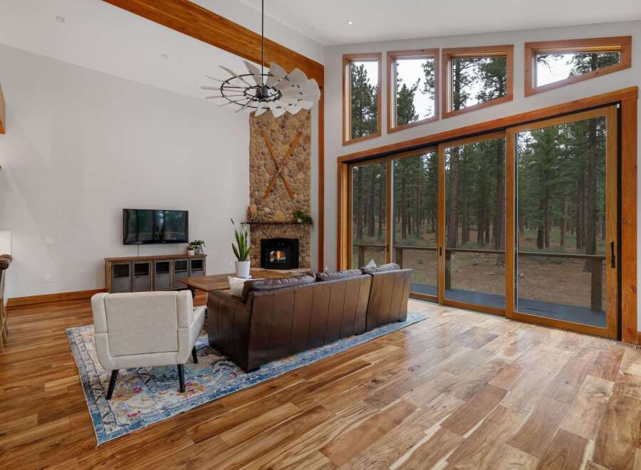 Experience luxury living in this stunning great room, featuring a floor-to-ceiling stone fireplace and expansive windows that showcase breathtaking forest views.