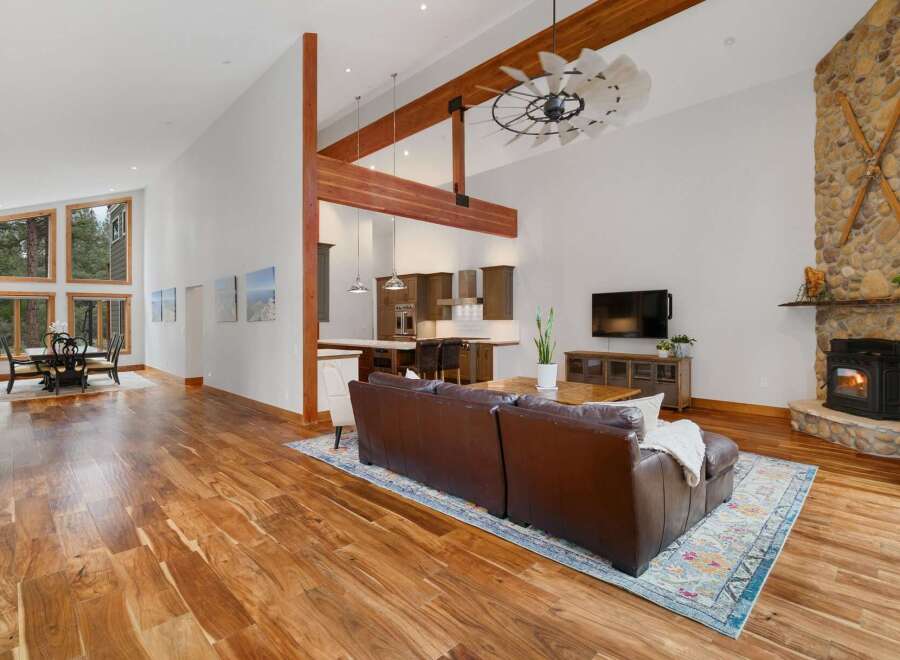Experience luxurious living in this stunning open-concept great room, featuring soaring vaulted ceilings with exposed wooden beams and a magnificent floor-to-ceiling stone fireplace.