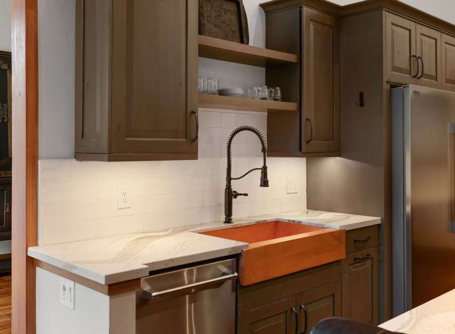 Experience luxury in this stunning kitchen featuring a striking copper farmhouse sink and elegant quartz countertops.