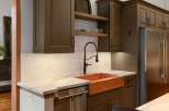 Experience luxury in this stunning kitchen featuring a striking copper farmhouse sink and elegant quartz countertops.