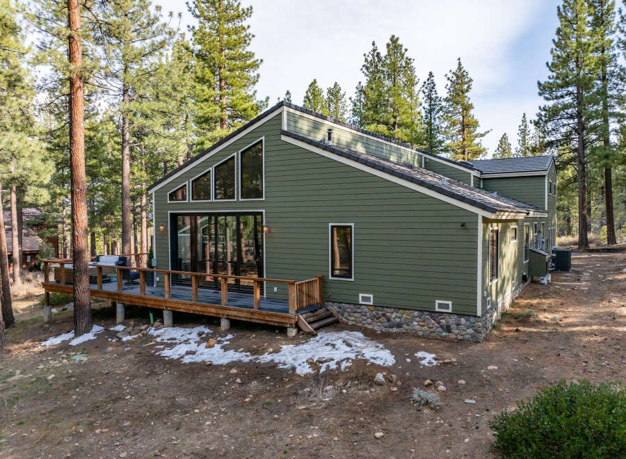 Nestled among tall pine trees, this charming home offers a serene retreat with its expansive wooden deck and modern green siding.
