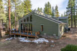 Nestled among tall pine trees, this charming home offers a serene retreat with its expansive wooden deck and modern green siding.