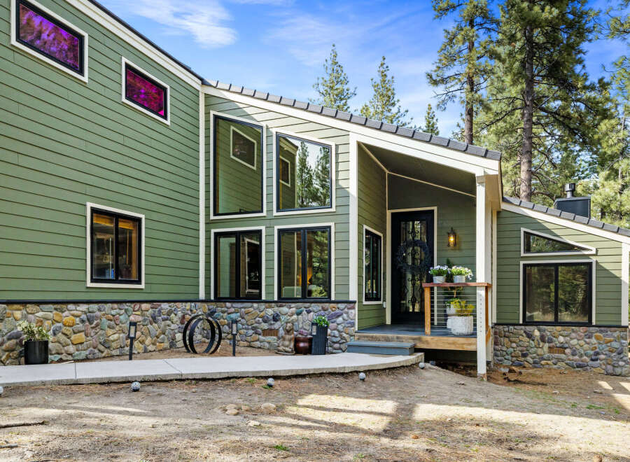 Discover this stunning modern home featuring a unique green siding and a striking stone foundation.
