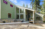 Discover this stunning modern home featuring a unique green siding and a striking stone foundation.