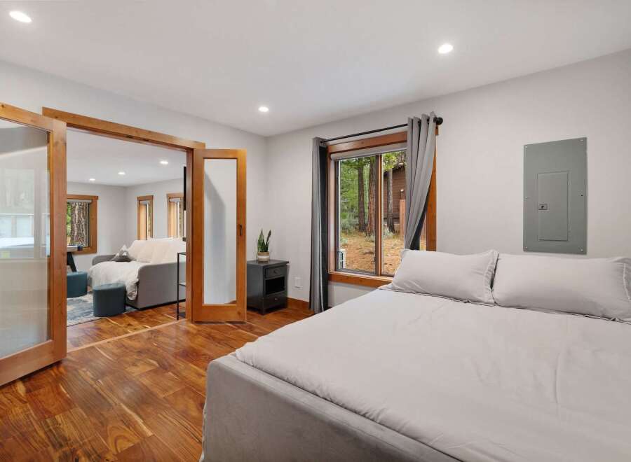 Experience serene living in this charming bedroom featuring a comfortable bed and a large window overlooking a lush forest.
