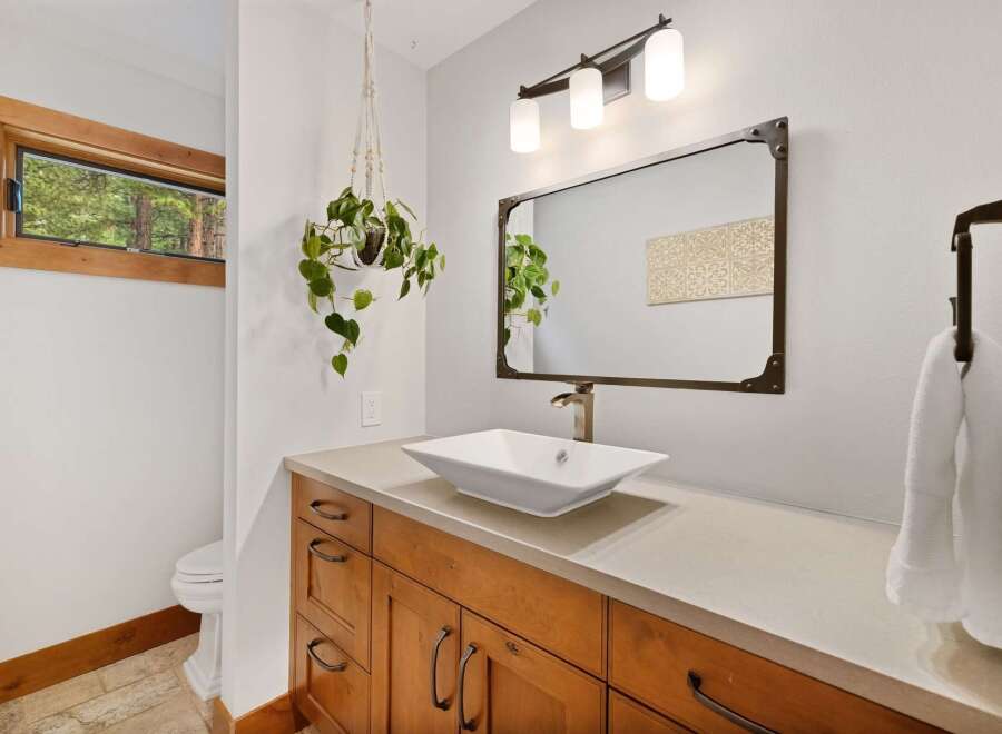 This modern bathroom features a sleek vessel sink atop a warm wood vanity, complemented by a decorative mirror and a stylish three-light fixture.