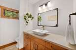 This modern bathroom features a sleek vessel sink atop a warm wood vanity, complemented by a decorative mirror and a stylish three-light fixture.