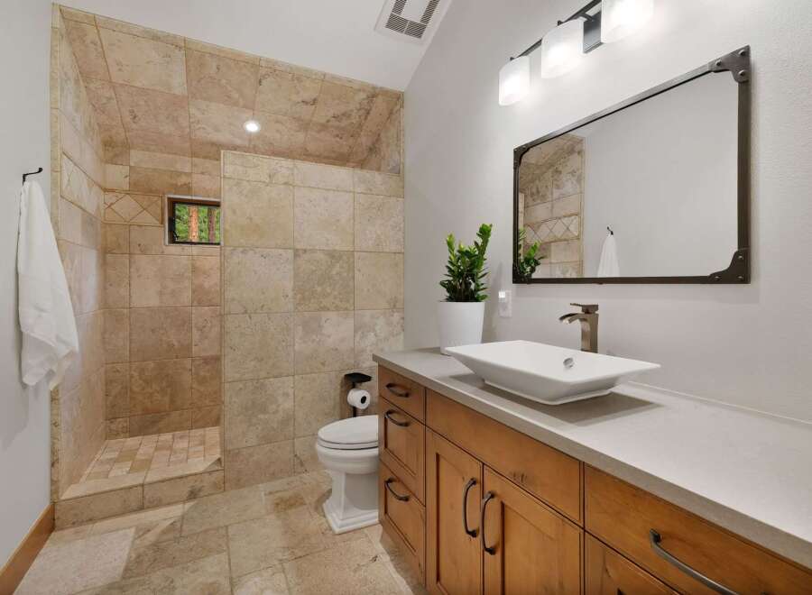 Experience luxury in this stunning bathroom featuring a spacious walk-in shower with elegant travertine tile and a charming window overlooking nature.