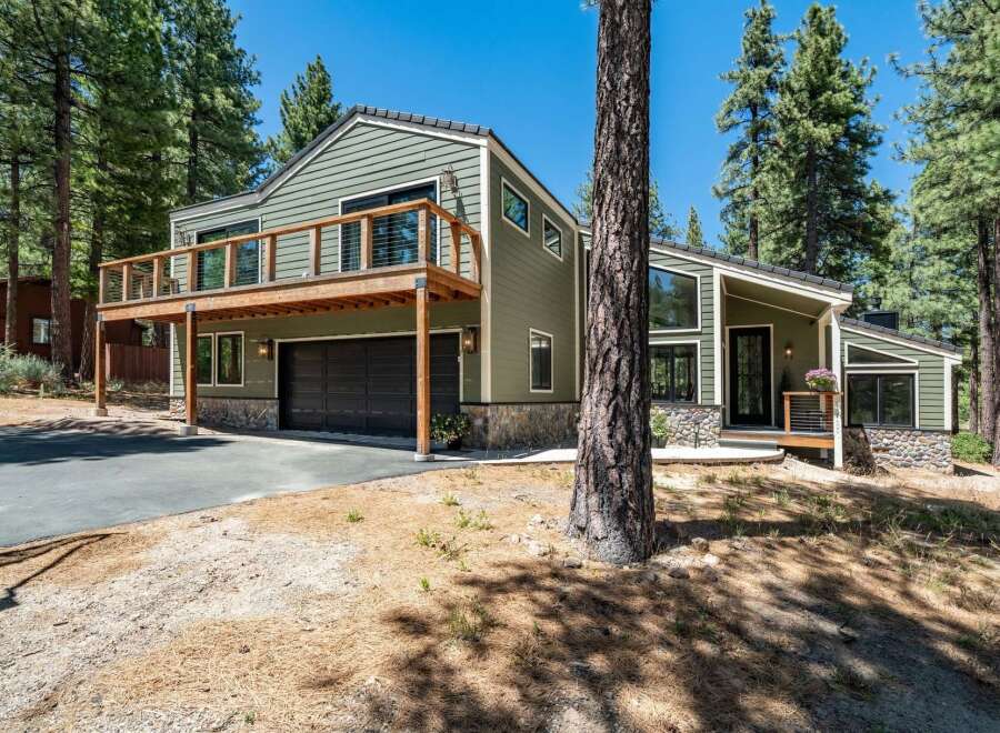 Nestled among tall pine trees, this modern home offers a unique architectural design with a striking green exterior and a spacious wooden deck.