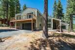 Nestled among tall pine trees, this modern home offers a unique architectural design with a striking green exterior and a spacious wooden deck.