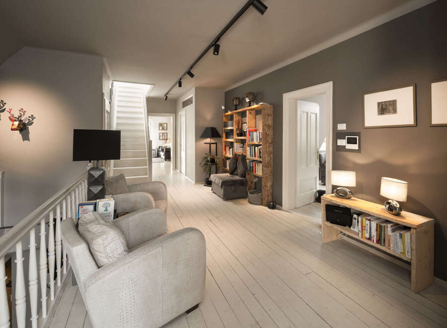 This spacious hallway features a modern track lighting system illuminating the white wooden floor and a staircase leading to the upper level.