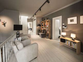 This spacious hallway features a modern track lighting system illuminating the white wooden floor and a staircase leading to the upper level.
