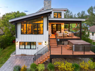 Experience luxury mountain living in this stunning modern home featuring expansive windows, a spacious deck with a hot tub, and an outdoor entertaining area with a grill.