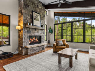 Experience rustic elegance in this living room, featuring a grand stone fireplace and expansive windows that frame breathtaking forest views.
