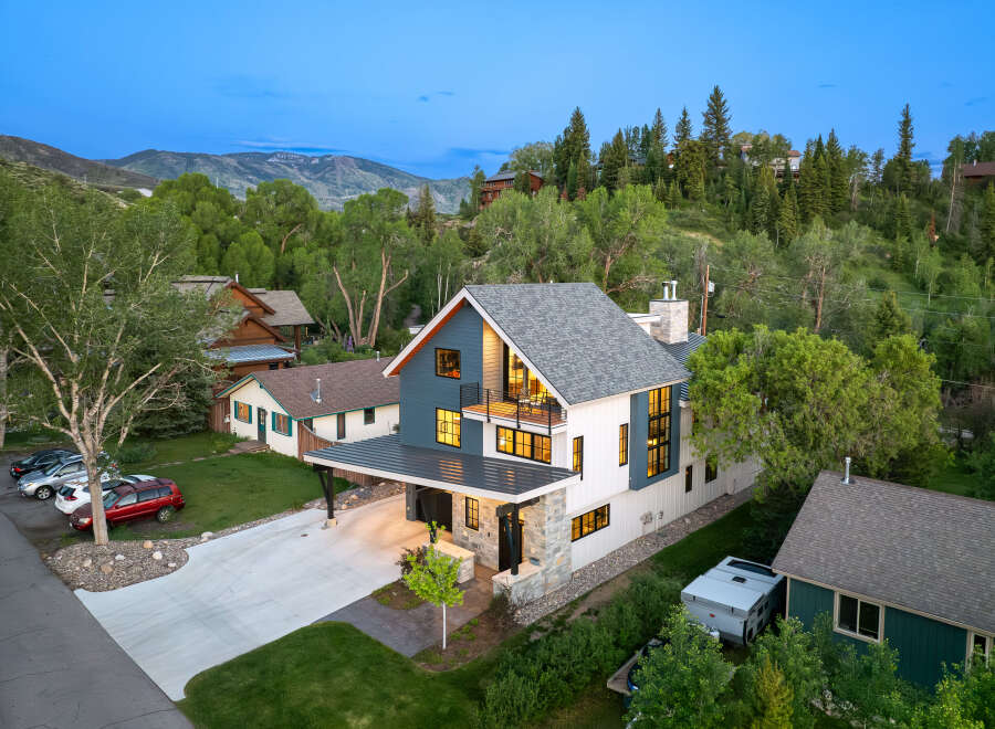 Experience modern mountain living in this stunning home, featuring a striking blue and white facade, expansive windows, and a spacious balcony perfect for enjoying the twilight views.