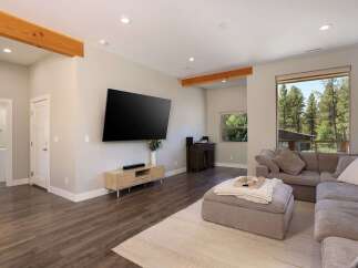 Experience modern living in this spacious great room, featuring exposed wooden beams and a large flat-screen TV mounted above a stylish media console.