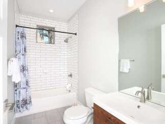This modern bathroom features a clean white subway tile shower and tub surround, complemented by a sleek wooden vanity and a large vanity mirror.